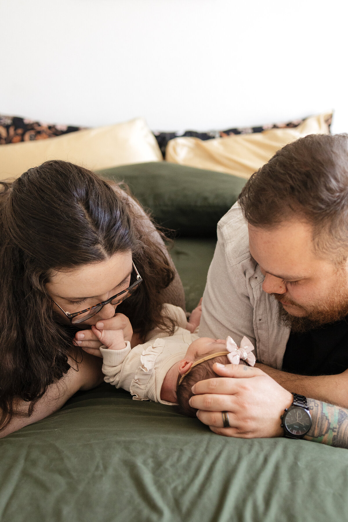 Longmont newborn laying on bed while parents lay next to her and mom kissing her little hand