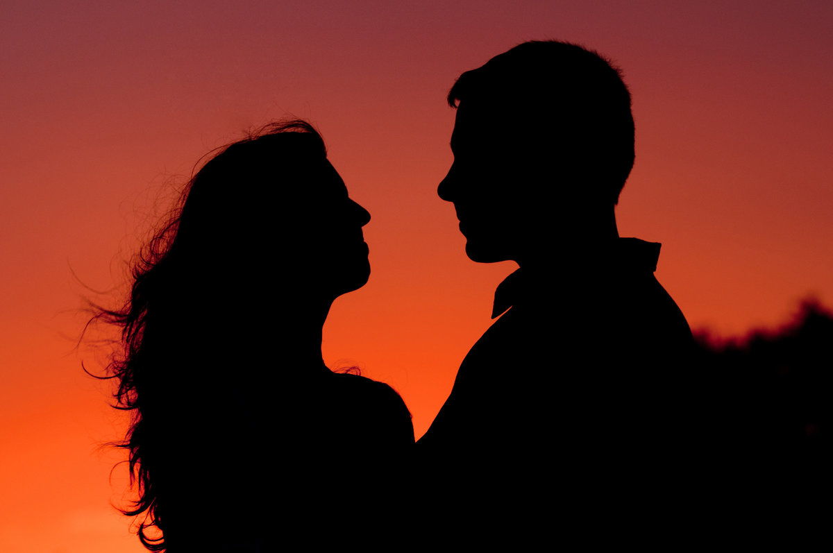 Engagement couple silhouetted  against a bright fire orange sunset sky