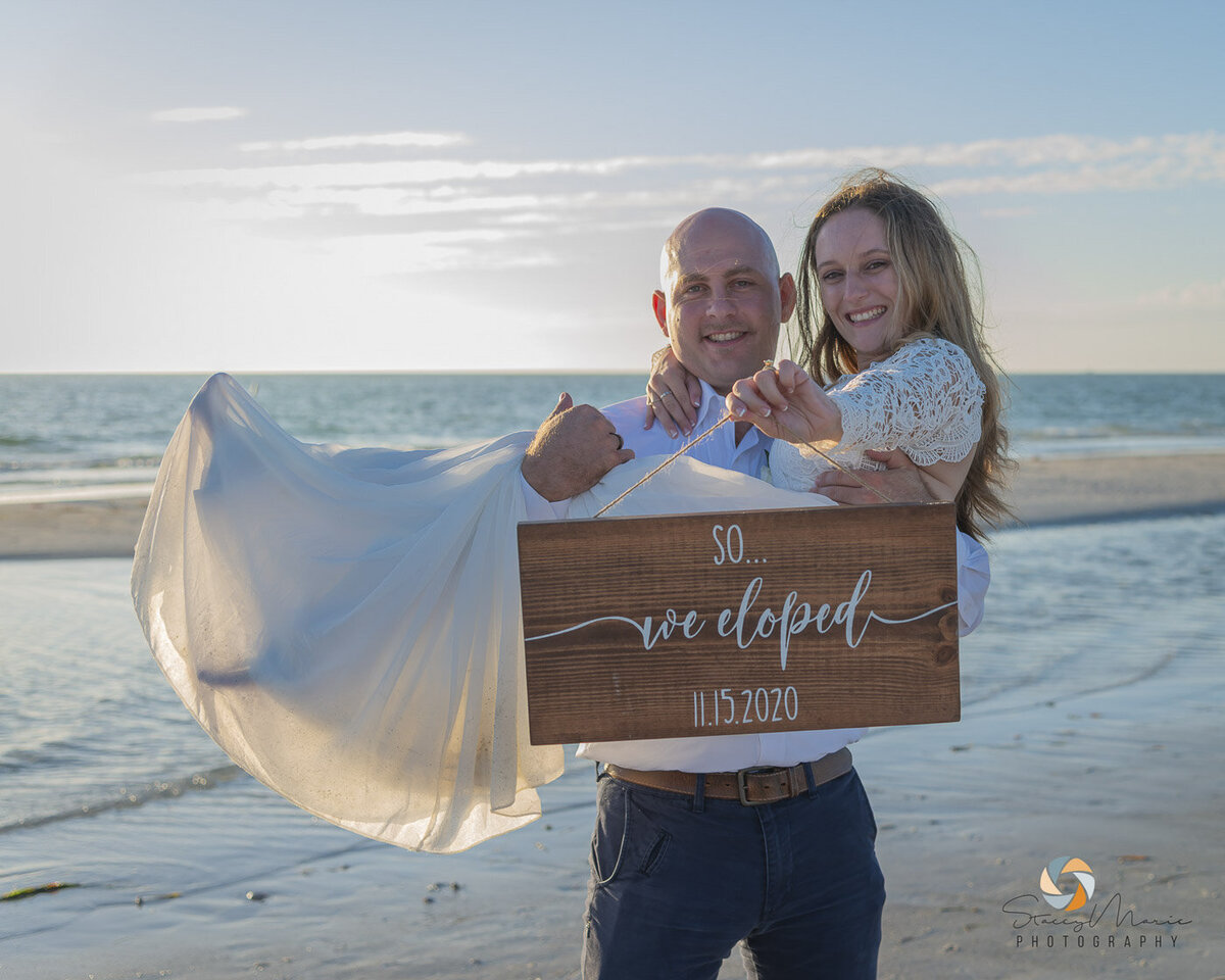 A groom holds his bride while she holds a sign stating their elopement date.