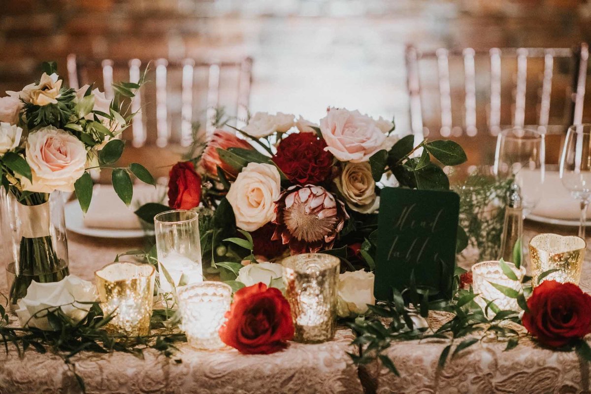 lush head table flowers in red, pink, blush, and greens, with candles, and clear Chivari chairs