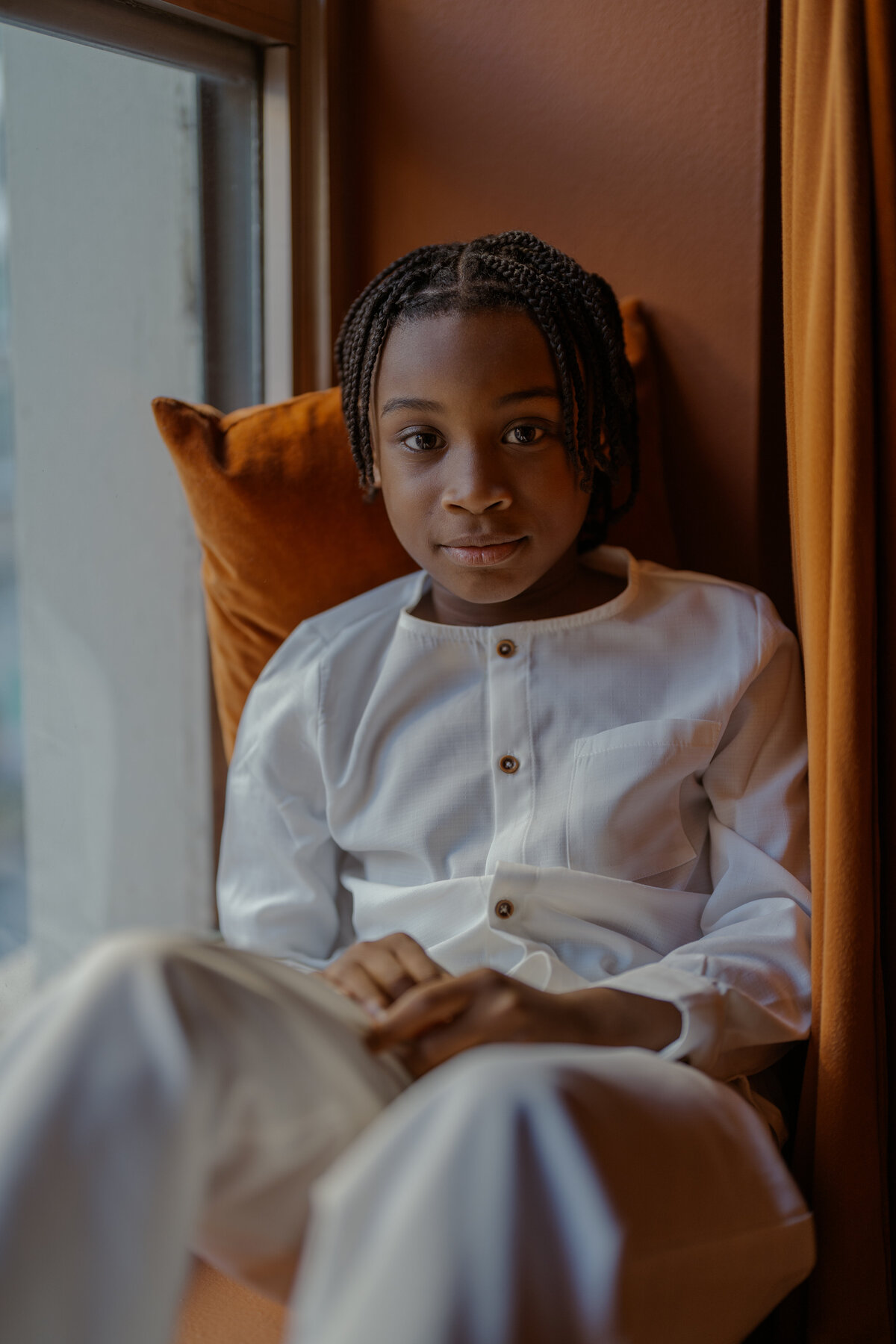 A portrait of a young boy sitting by the window with a calm and relaxed expression, showcasing the essence of fine art family photography during an NYC session.