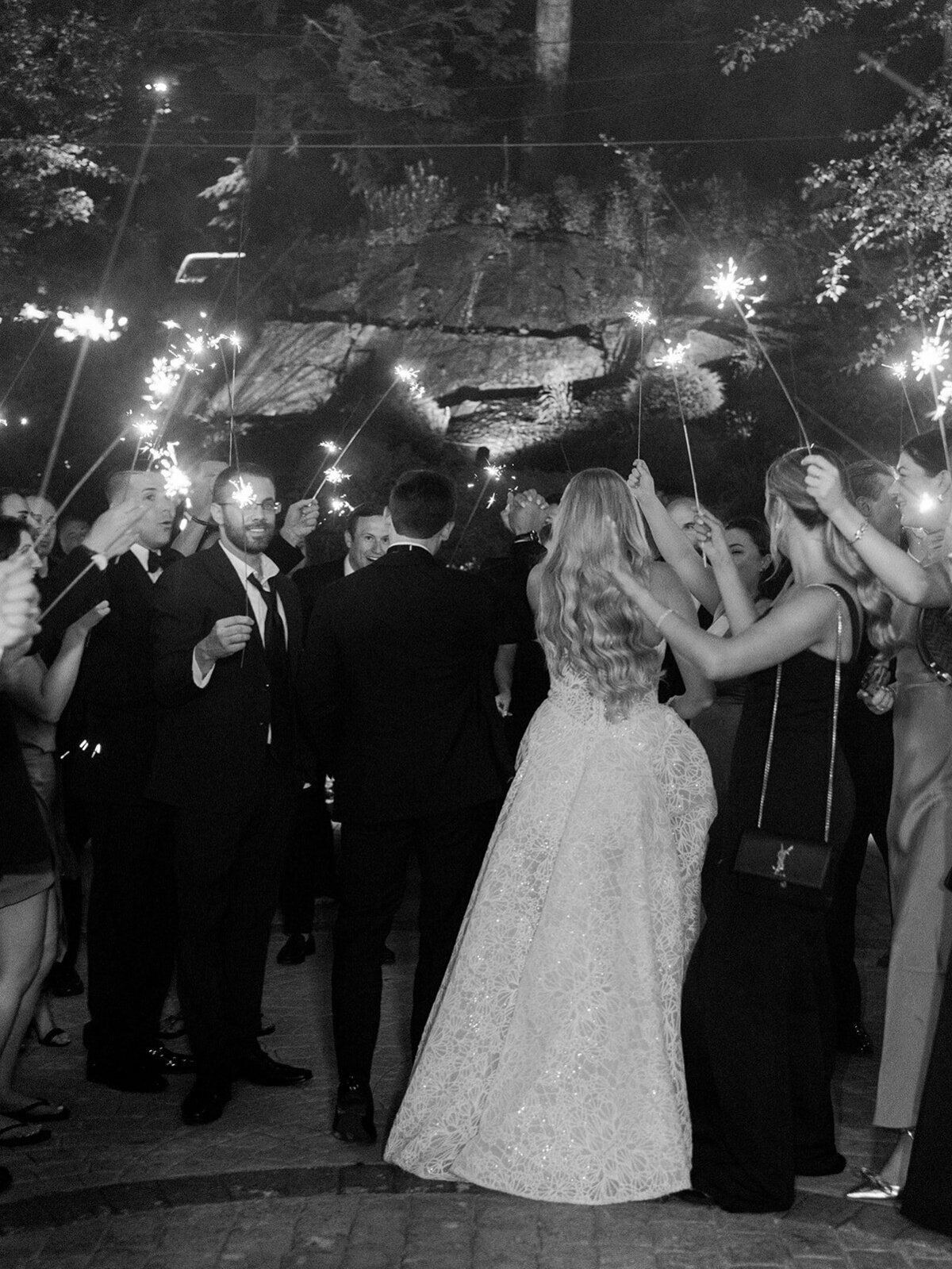 Bride and groom from the back of their sparkler exit surrounded by their friends and family.