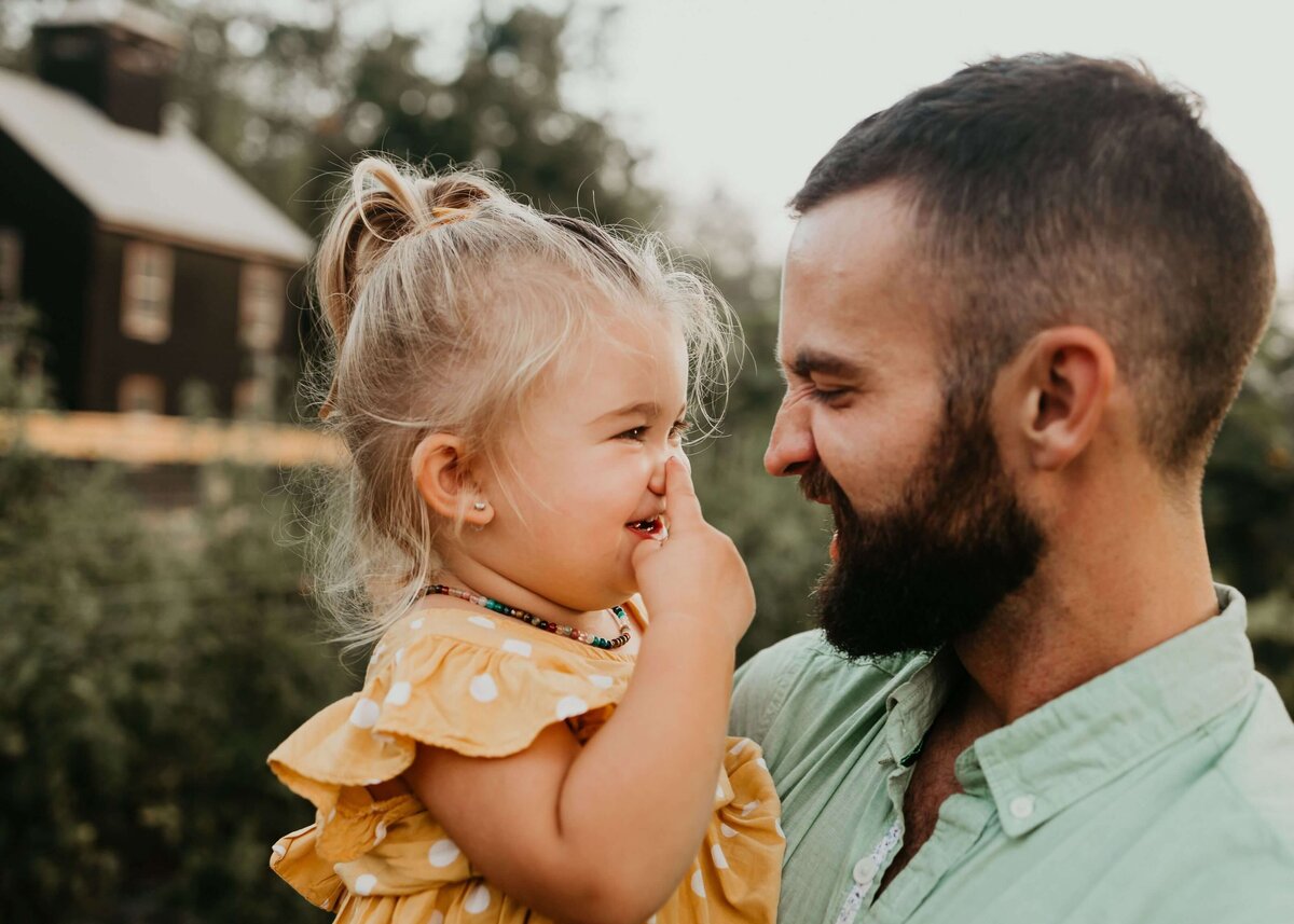 A man with a beard and a little girl in front of a farm captured by a Pittsburgh family photographer.