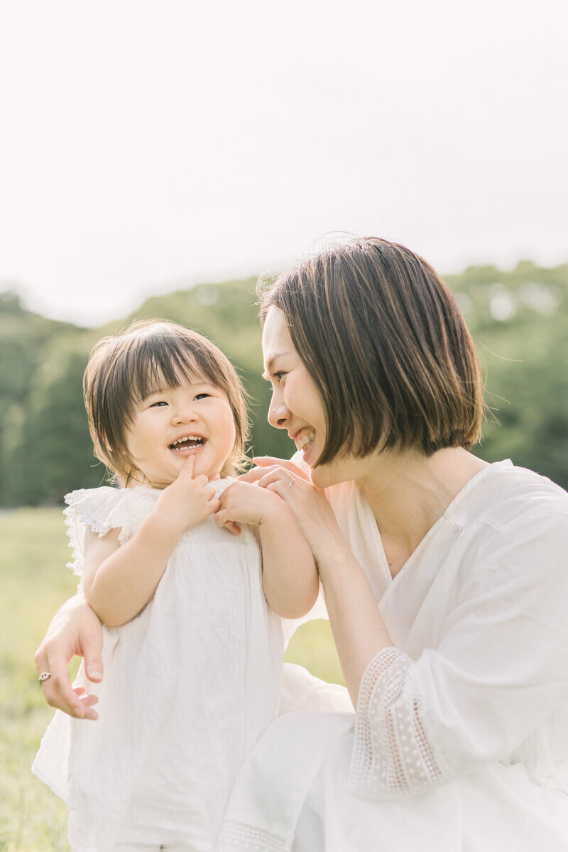 A daughter and mother smiling as the mother pokes the girl's cheek. They both are wearing white dresses, beautifully styled. Shot in Shibuya by Yukika Ishikawa Photography.