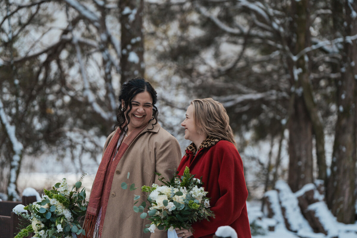 Lesbian women walk down a snowy path on their winter elopement day 