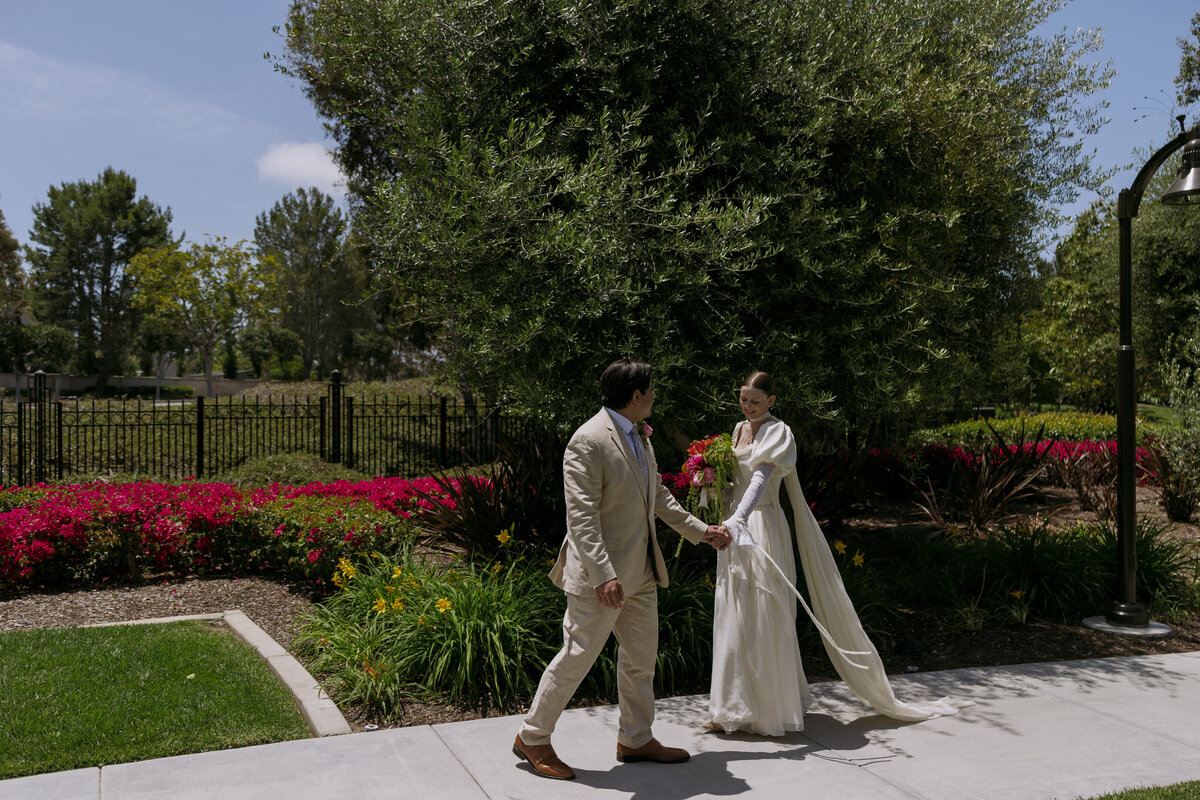 Yered holding Regan's hand and leading her forward as they walk.
