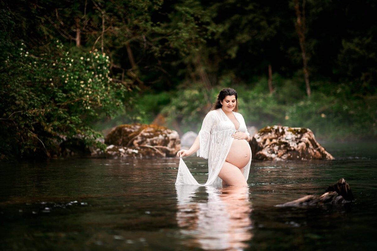 Pregnant woman in white lace robe posing in the river at Golden Ears Park in Maple Ridge