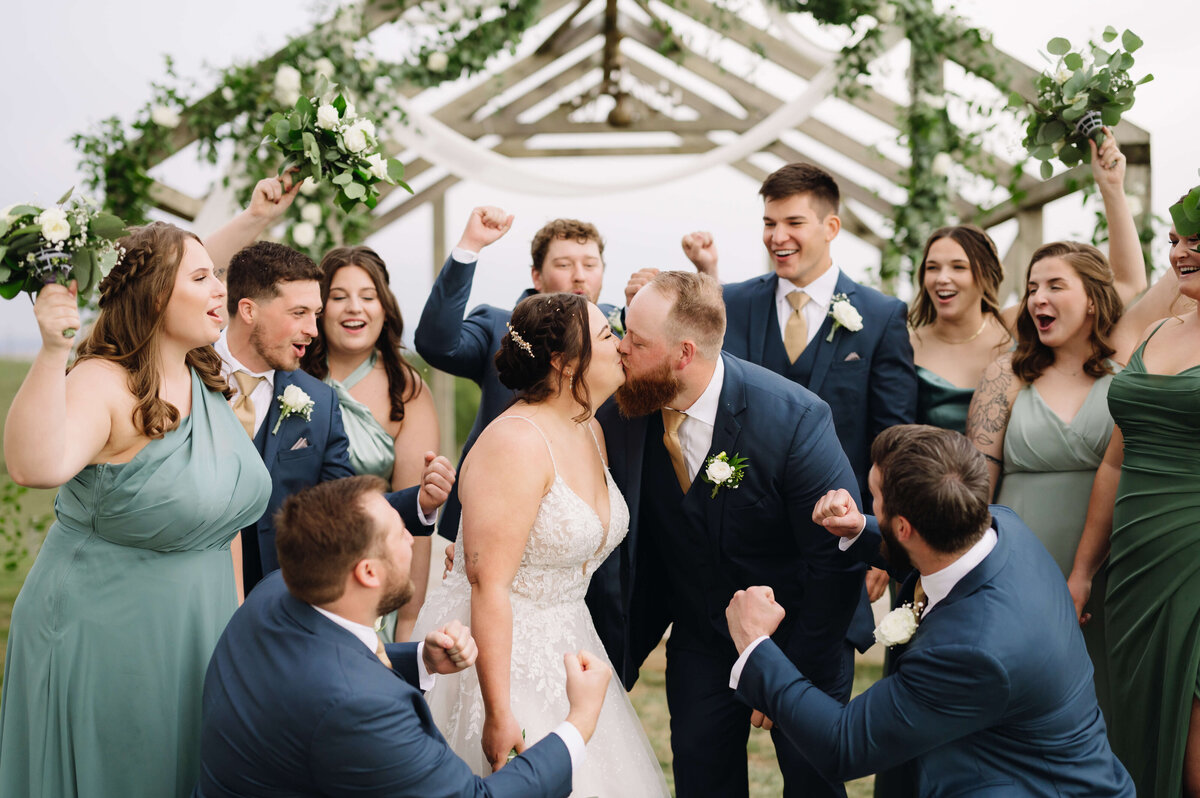 bride adn groom kiss while their bridal party dances and cheers around them at their outdoor wedding ceremony space