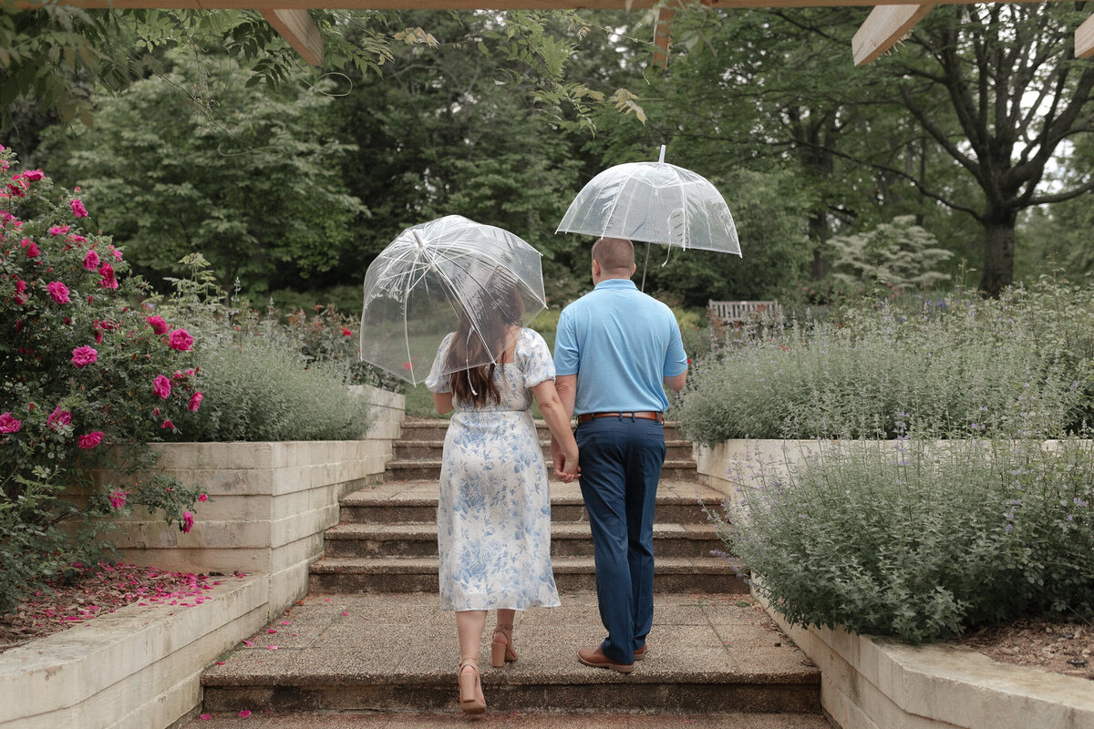 couple holding hands with umbrellas in garden with flowers