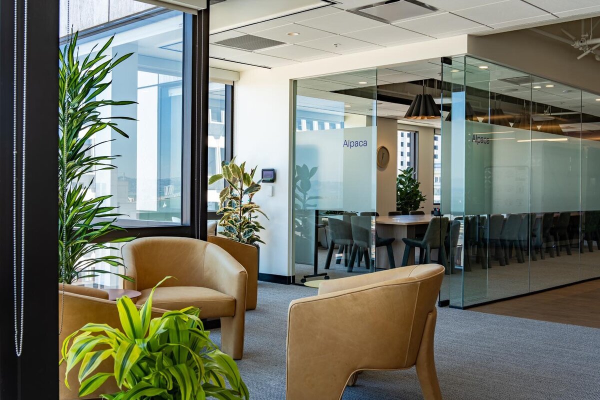 Quiet seating nook with tan leather chairs, large windows, and potted plants overlooking the city.