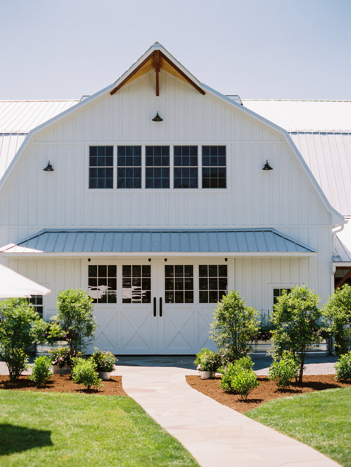 Exterior photo of the Groom in a pink jacket and bride in an elegant dress posing for a portrait at Wildflower On Watts white barn venue