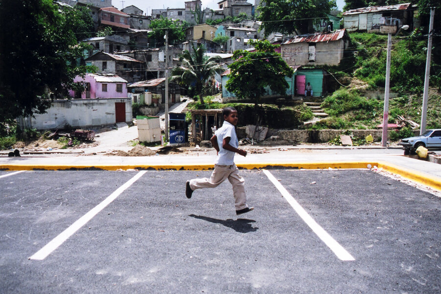Child skips across parking lot in La Zurza with shanty town in background