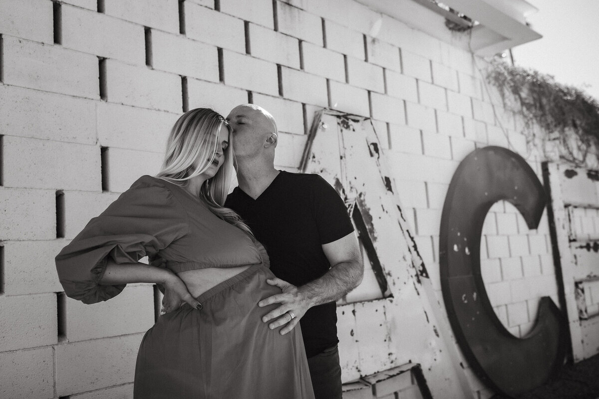 Palm Springs babymoon photography session at Ace Hotel. Husband kisses wife with hand on belly with Ace sign behind. Photo in black and white