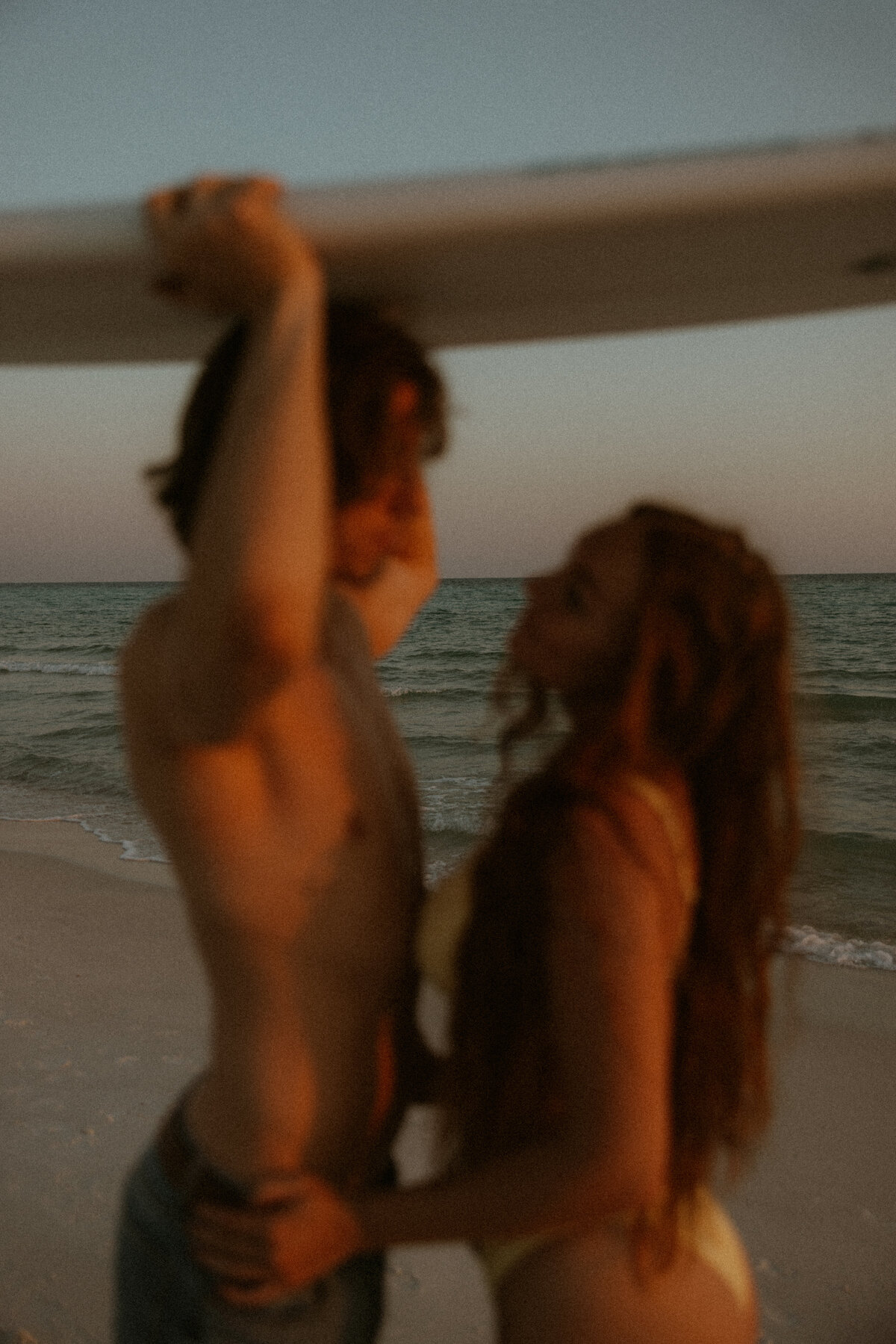 couples standing under surfboard