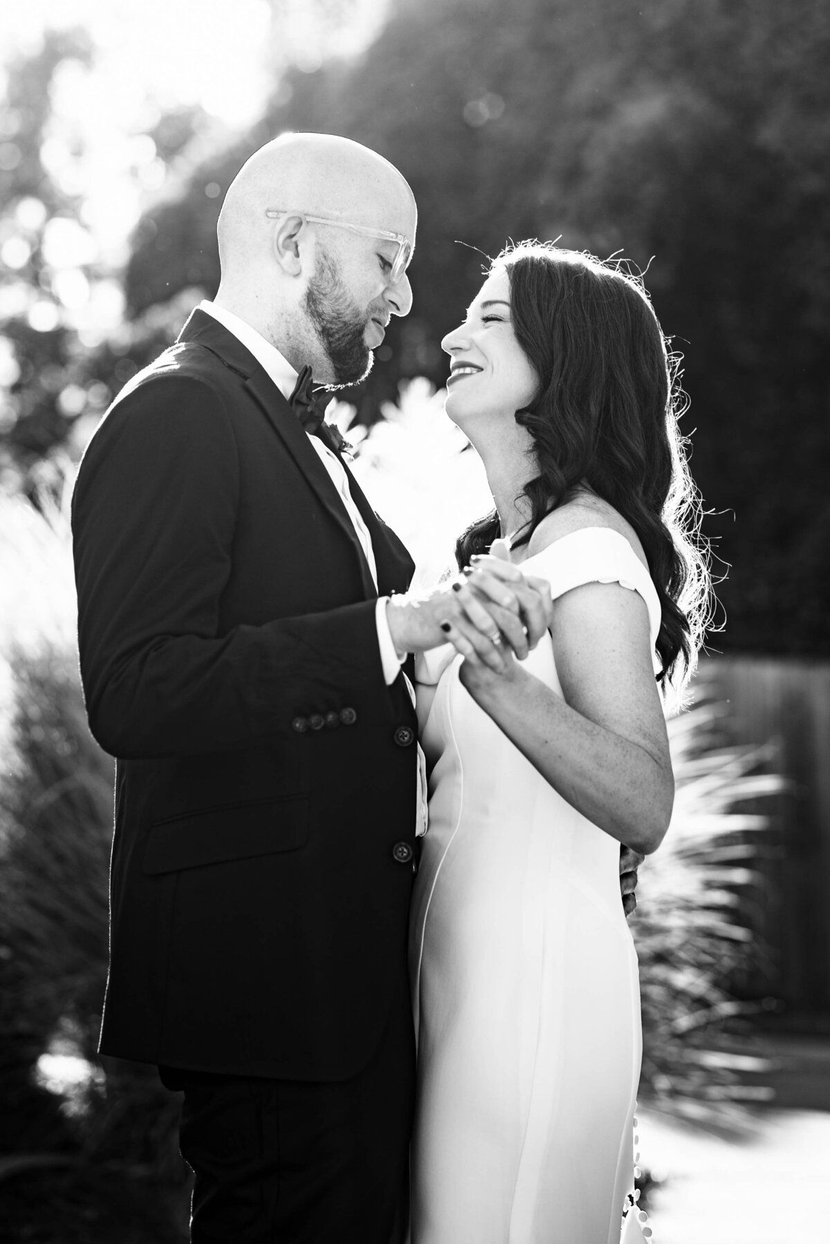 Black-and-white-photograph-of-bride-and-groom-holding-hands-dancing-and-smiling-at-one-another-outside-Eventide-Brewing-in-Atlanta