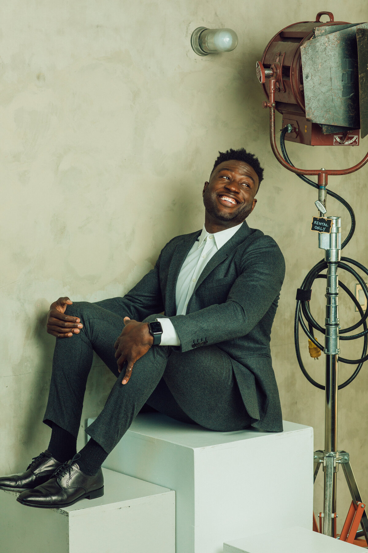 Portrait Photo Of Young Black Man In Gray Suit Seated In a White Box Los Angeles