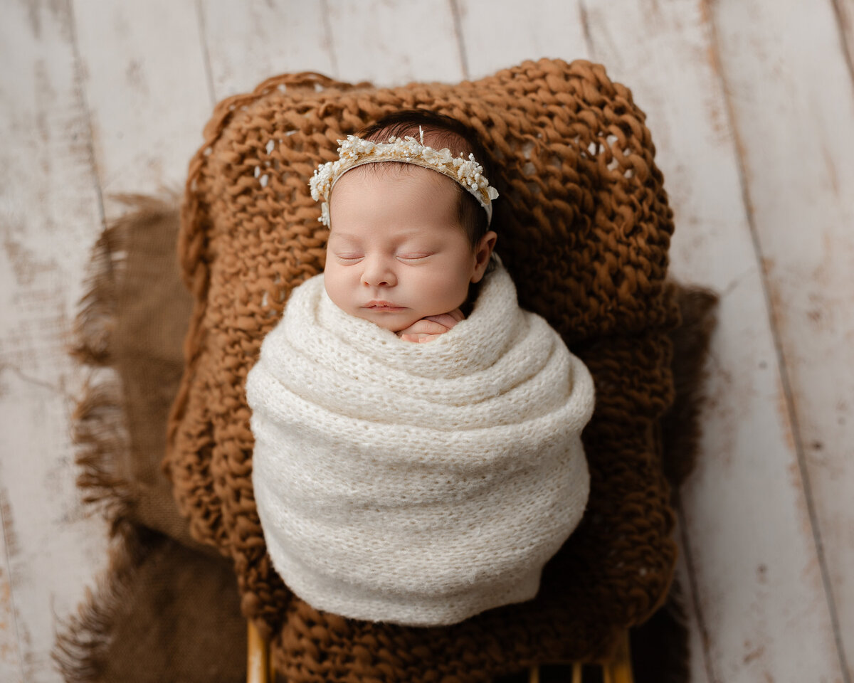 Newborn baby girl wrapped in soft, creamy knits with a delicate floral crown, resting peacefully on a cozy knitted backdrop. Captured during a beautiful newborn session by Kaitlyn Dawn Photography in the Inland Empire.