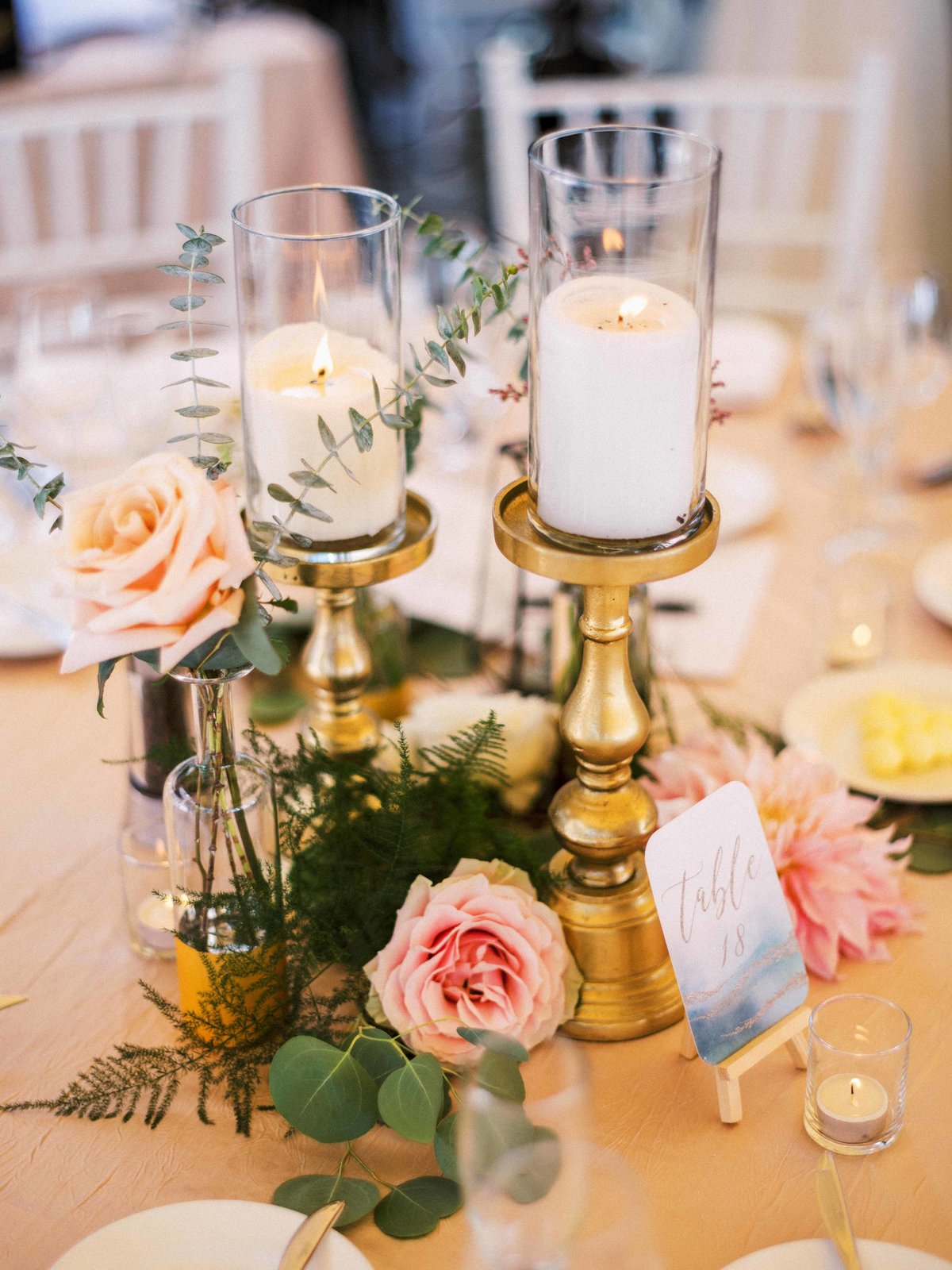 Bud vases and gold pillar candles are nestled into greenery and flowers