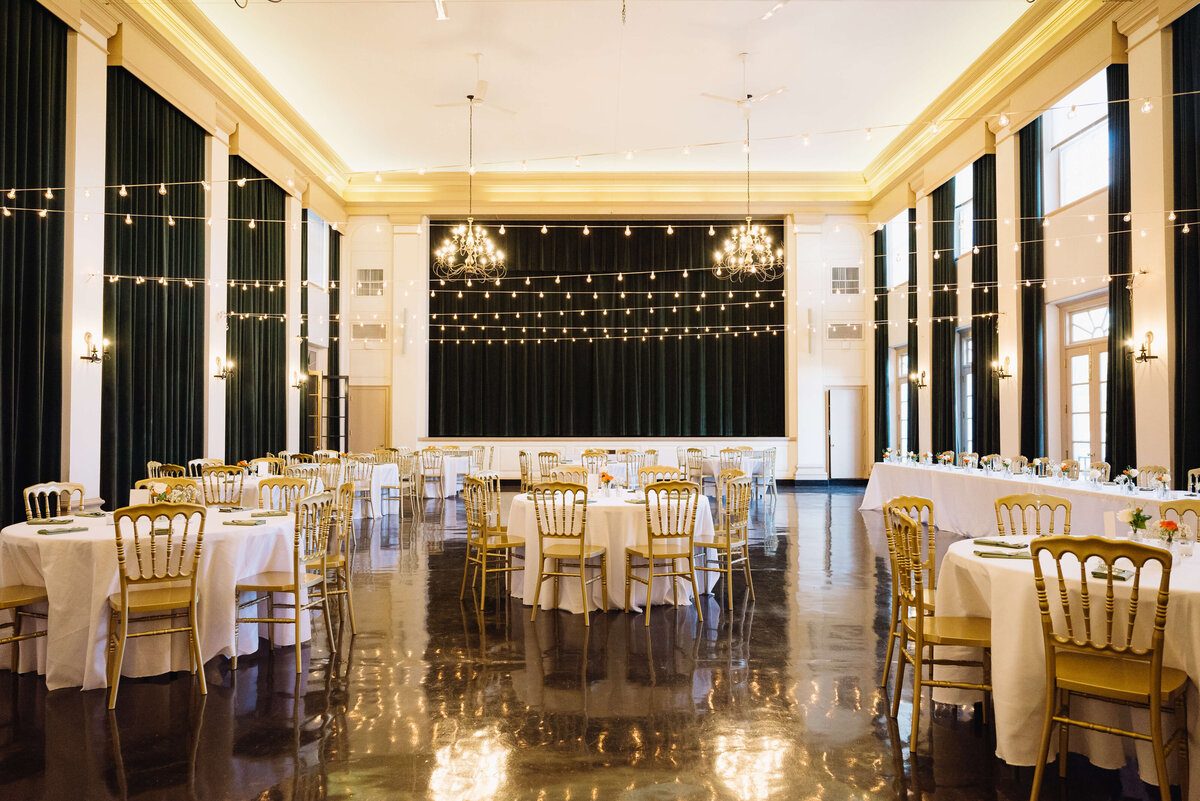 indoor wedding reception decor with fairy lights overhead and gold accents through the tablescapes at middleburg community center