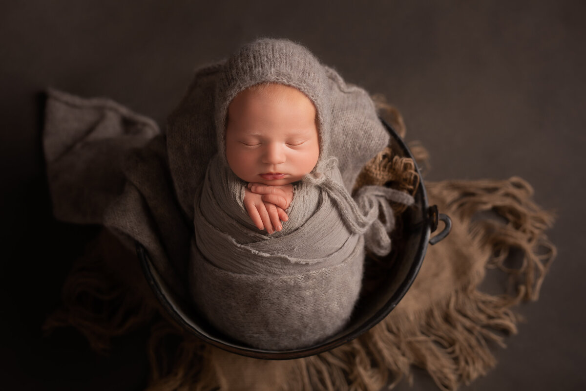 Newborn baby wrapped in a grey wrap & posed in a bucket