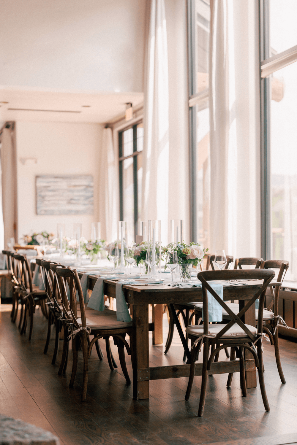 Summer wedding reception setup with wooden farm tables, pastel floral centerpieces, and light blue napkins at Moonlight Basin.