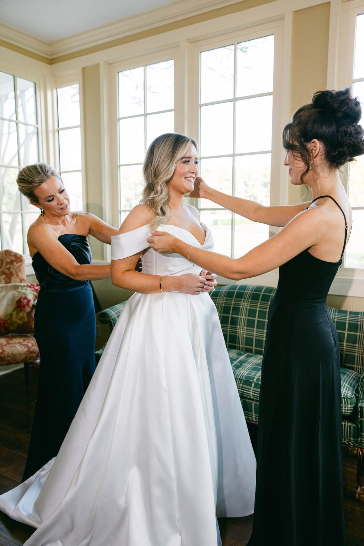 A wedding day photo of the brides mom and sister adjusting her wedding dress