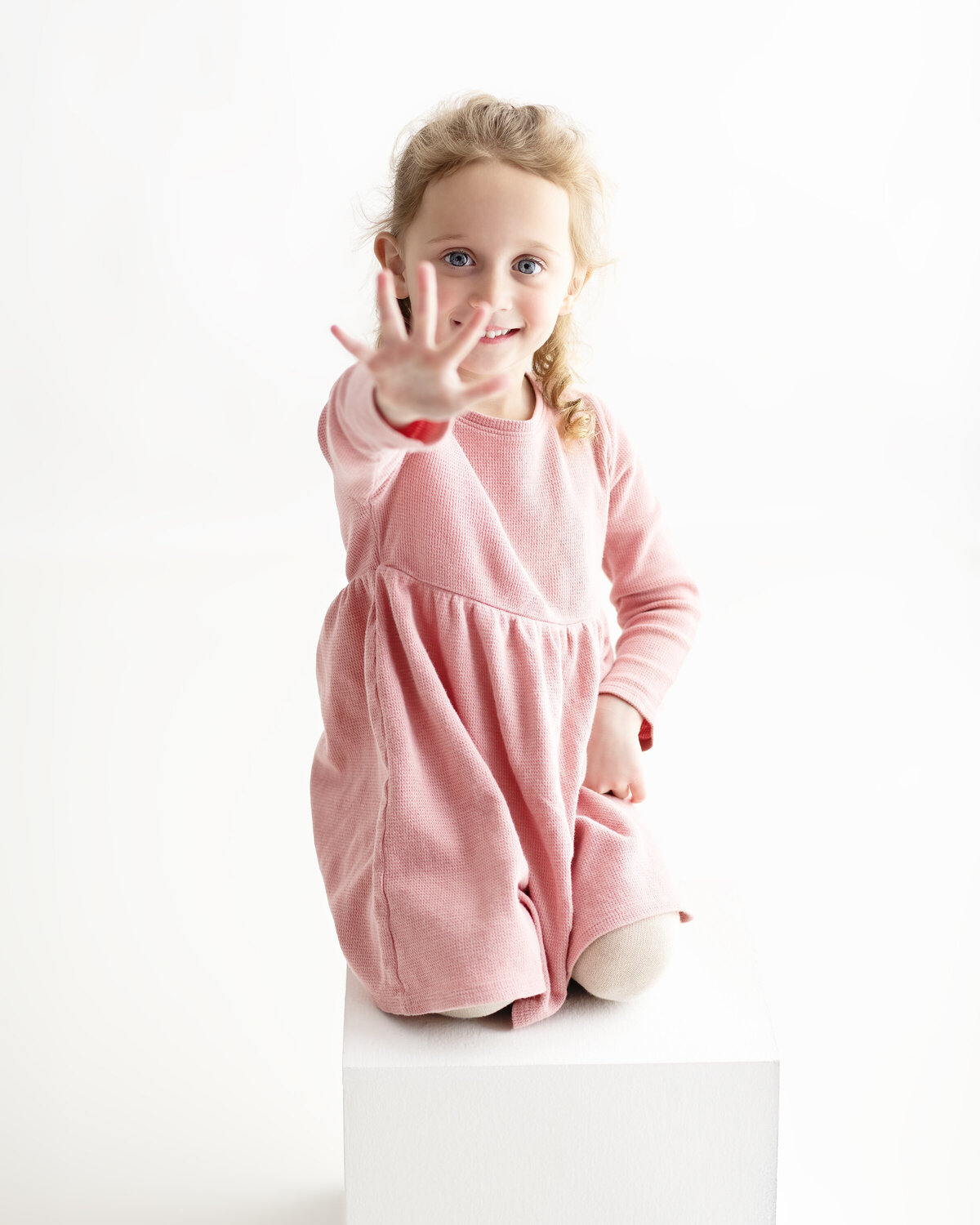 Studio milestone portrait of a smiling girl showing five fingers—celebrating her fifth birthday with confidence and charm.
