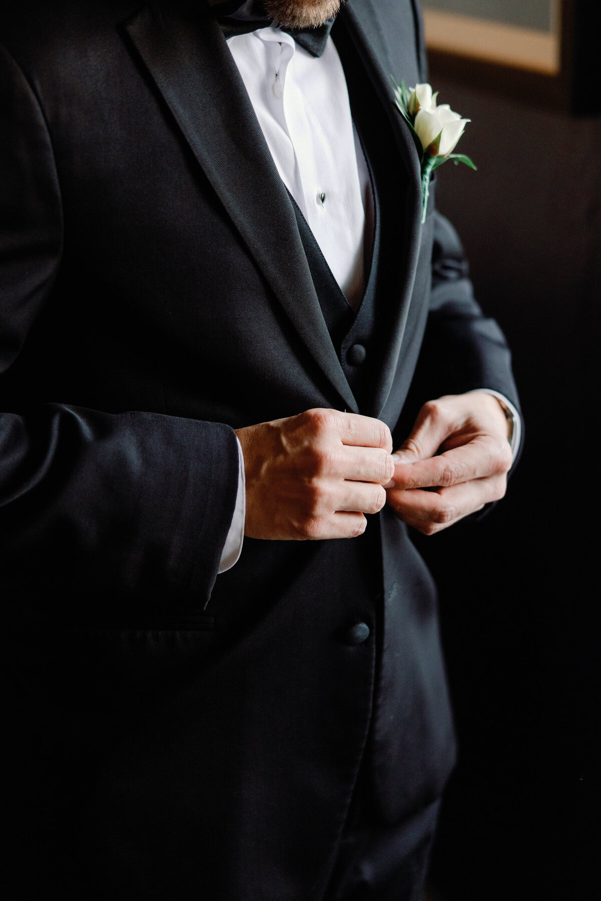 A closeup of a groom's hands as he buttons up his wedding suit jacket