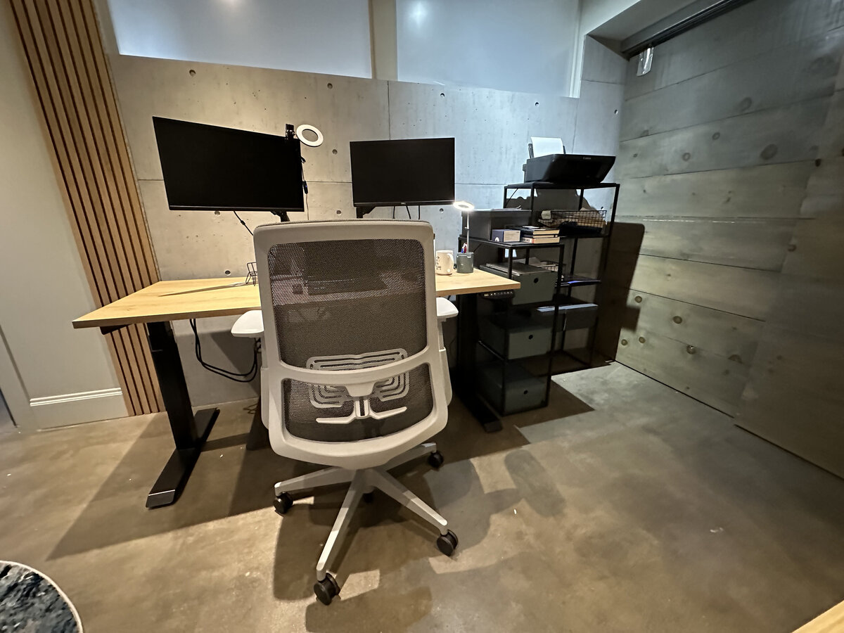 Modern industrial home office workspace with dual monitor desk setup, ergonomic office chair, concrete floors and textured walls with faux concrete and oak slats in Westboro, Ottawa by Urbanomic Interiors. 