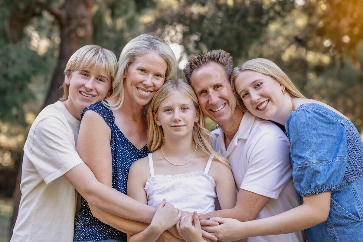 A family of five with blonde hair, wrapping their arms around each other and putting their heads together, smiling at the camera at Jeffrey Open Space in Irvine.