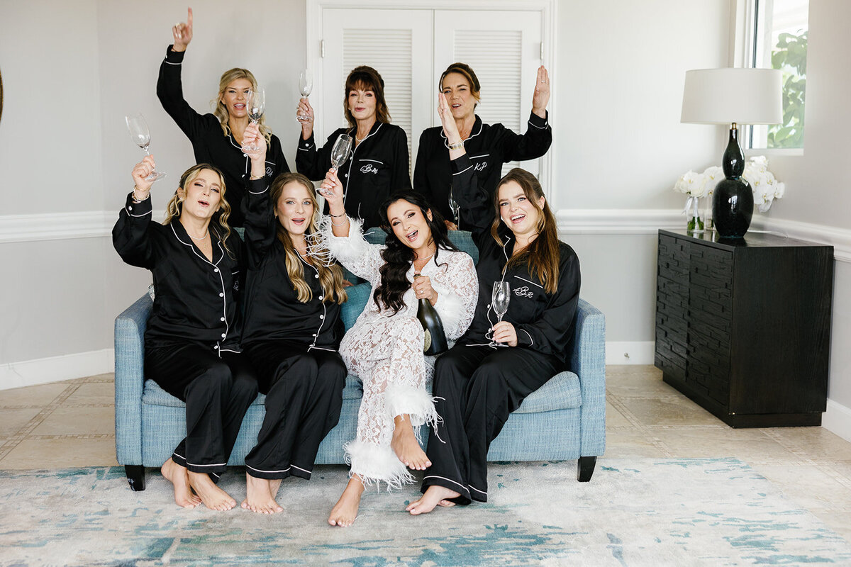 The bride and her bridesmaids toasting with champagne glasses in matching pajamas, celebrating during Ashley and Cameron's micro wedding at Ocean Reef in Key Largo, captured by Claudia Amalia Photography.