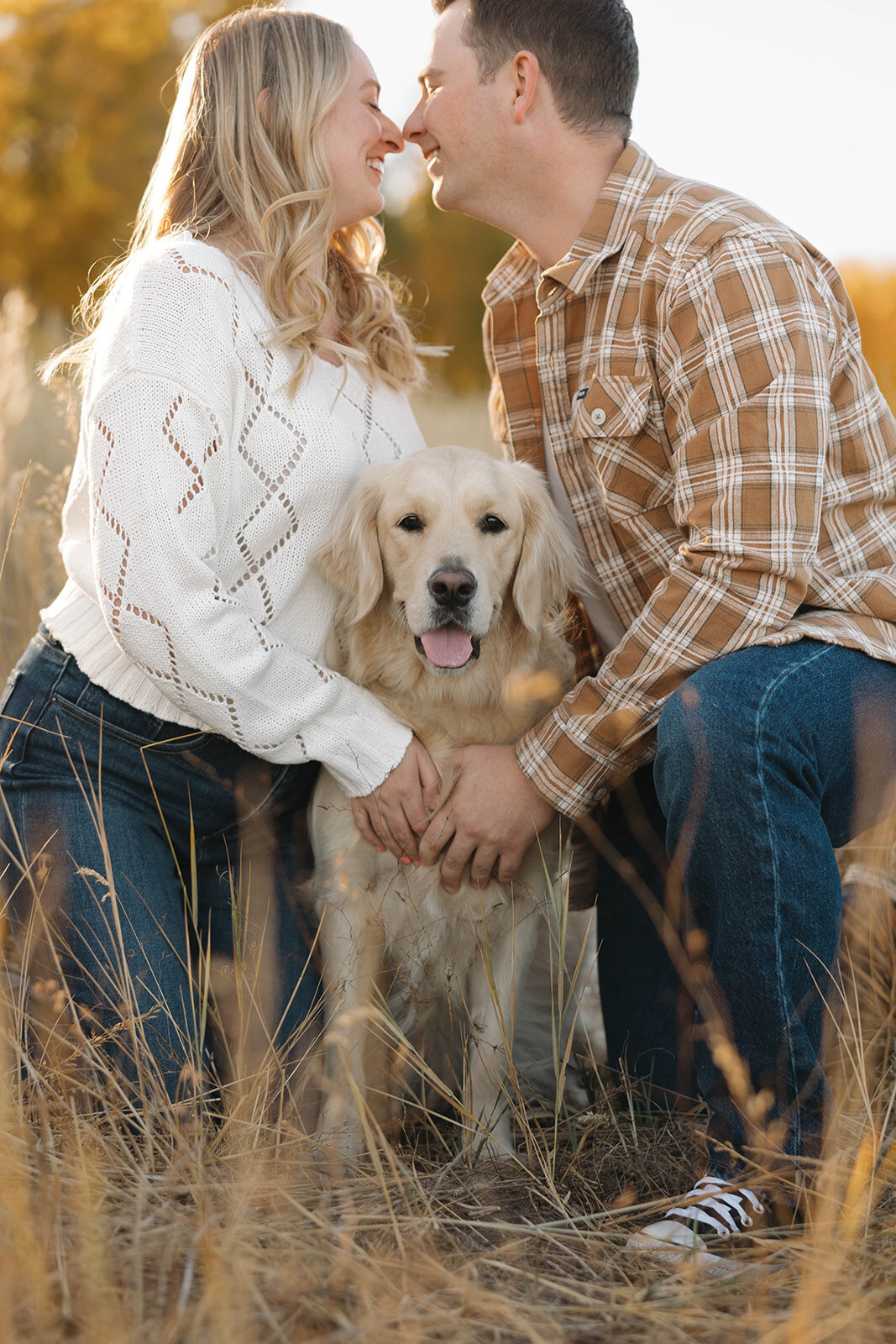 Couple snuggling with their golden retriever in the fall leaves