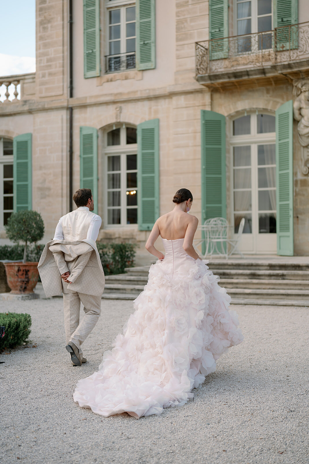 Bride and groom walking hand-in-hand across gravel courtyard in front of Château de Tourreau.
