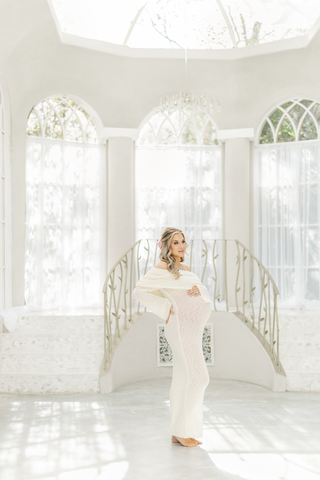 pregnant mom holds belly walking down staircase at the oak atelier studion in conroe for houston maternity photographer allie nichols photography