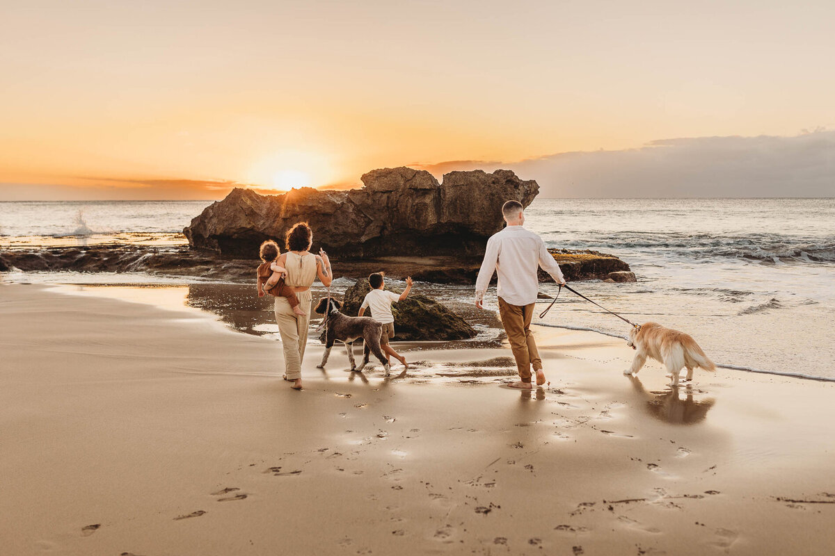 Family walking along Oahu beach at sunset with their dogs — warm and candid Hawaii family photography by Leslie Carbajal capturing connection and golden light