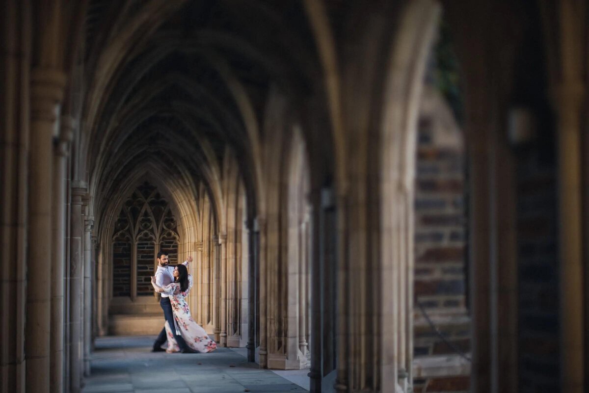A couple shares an intimate moment in a dimly lit gothic-style cloister, with emphasis on the architectural details