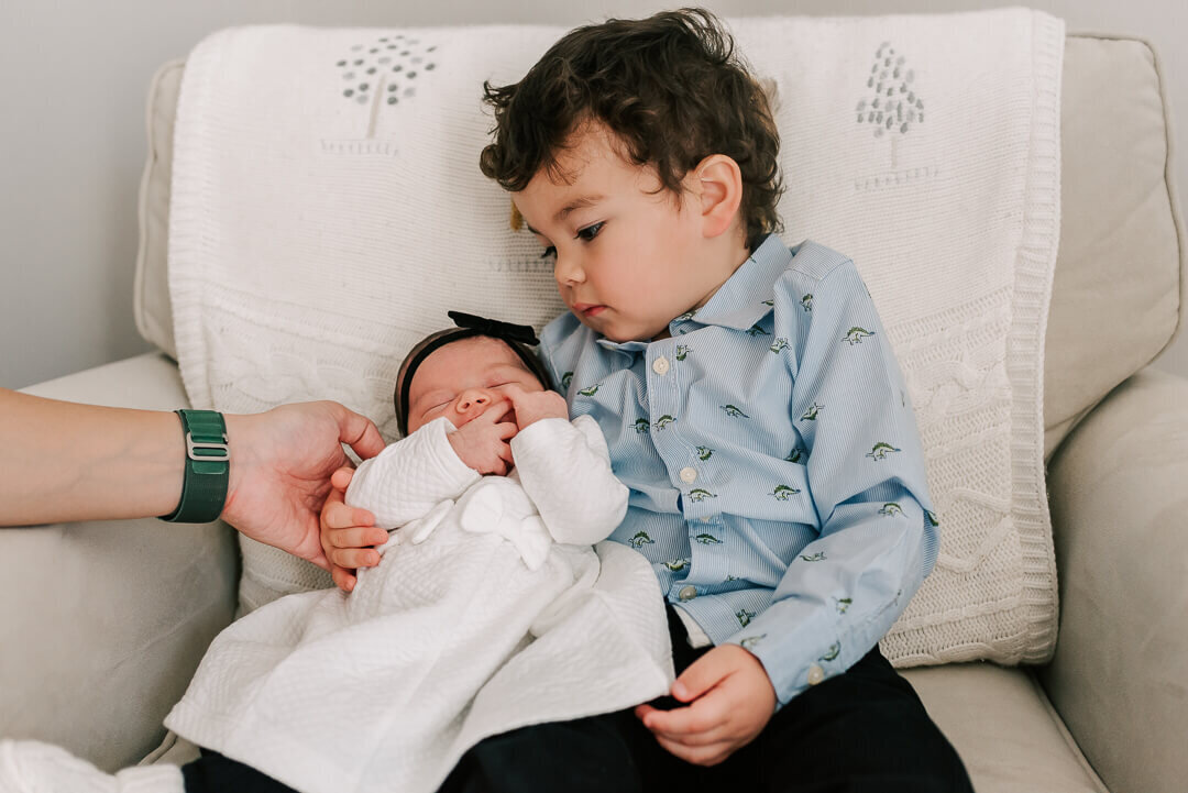 A big brother holds his baby sister and looks at her in awe, taken by Denise Van Photography