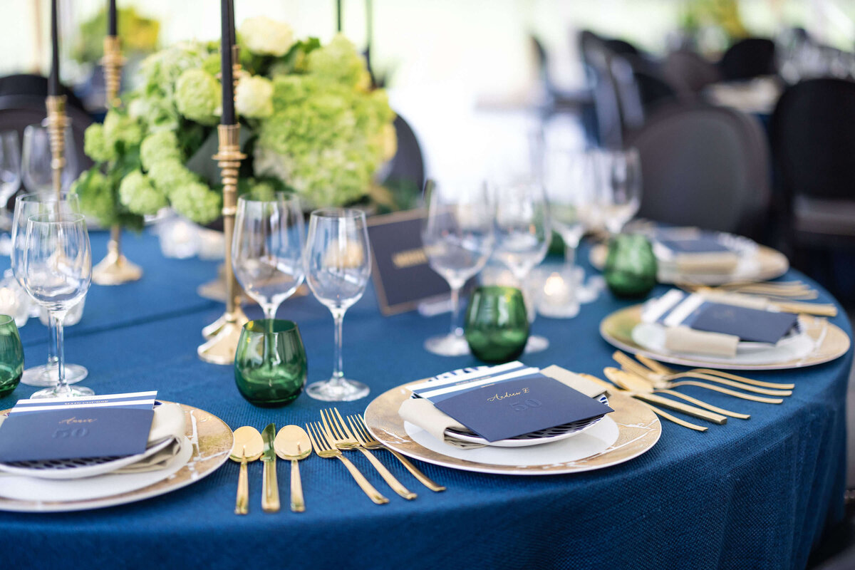a round dinner table laid in navy blue linen with navy blue menus and gold tableware for a 50th birthday party at avington park