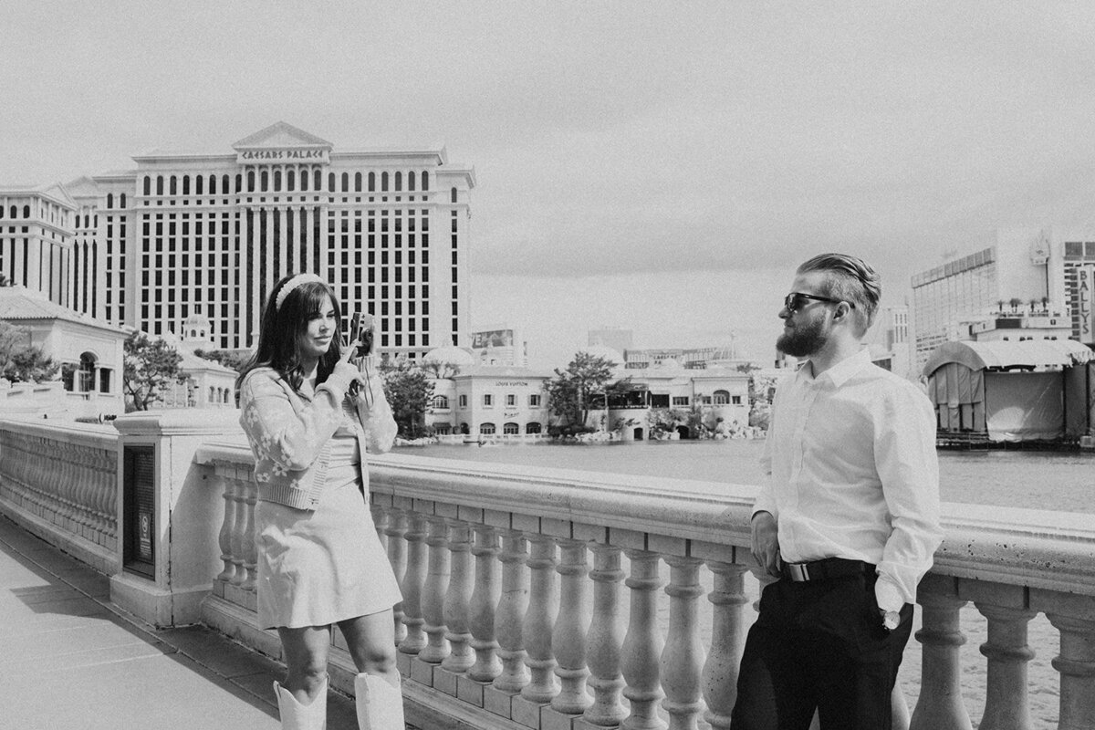 Person wearing skirt and floral cardigan points film camera at their partner who poses in front of caesars palace