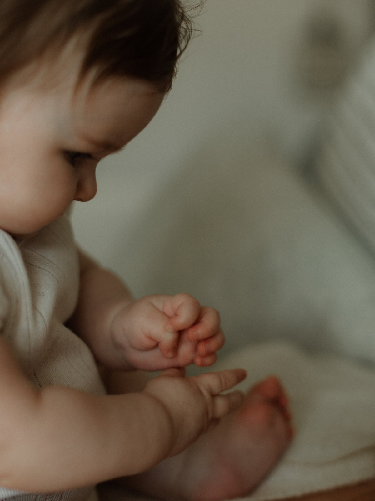 Close-up of a baby sitting in soft light highlighting the details of tiny fingers.