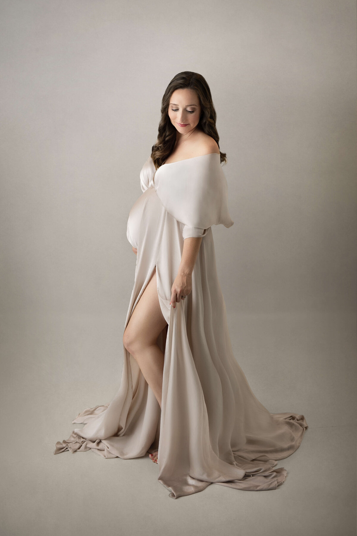 pregnant mom wearing a cream flowey maternity gown  in a photography studio at a maternity session