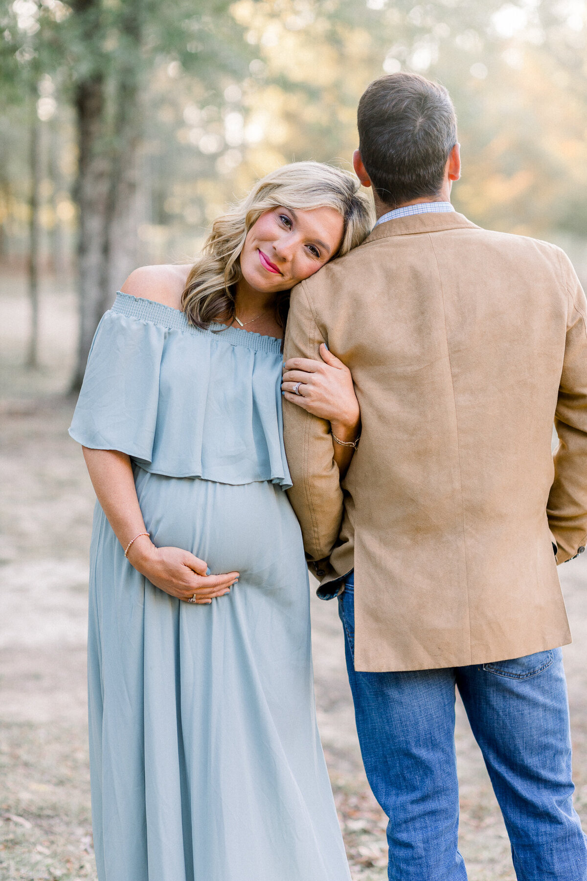 Mom to be wearing light blue dress posing with husband in an outdoor field by Brandon , MS Photographer