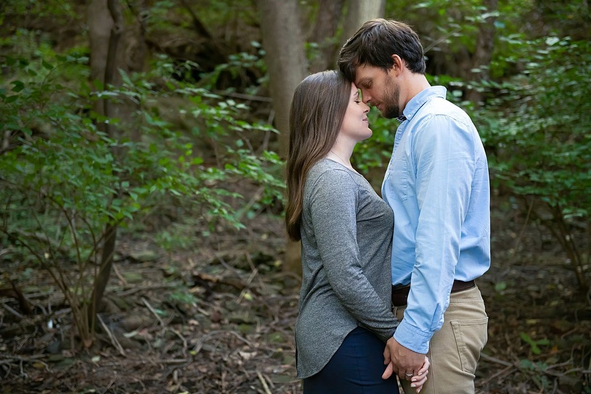 Romantic moment for an engaged couple standing forehead to forehead during their engagement session in a wooded area in Pittsburgh, PA