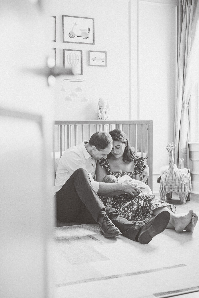 parents sit in front of a crib in their baby's nursery in this black and white shot captured by a newborn photographer in Leander, TX.