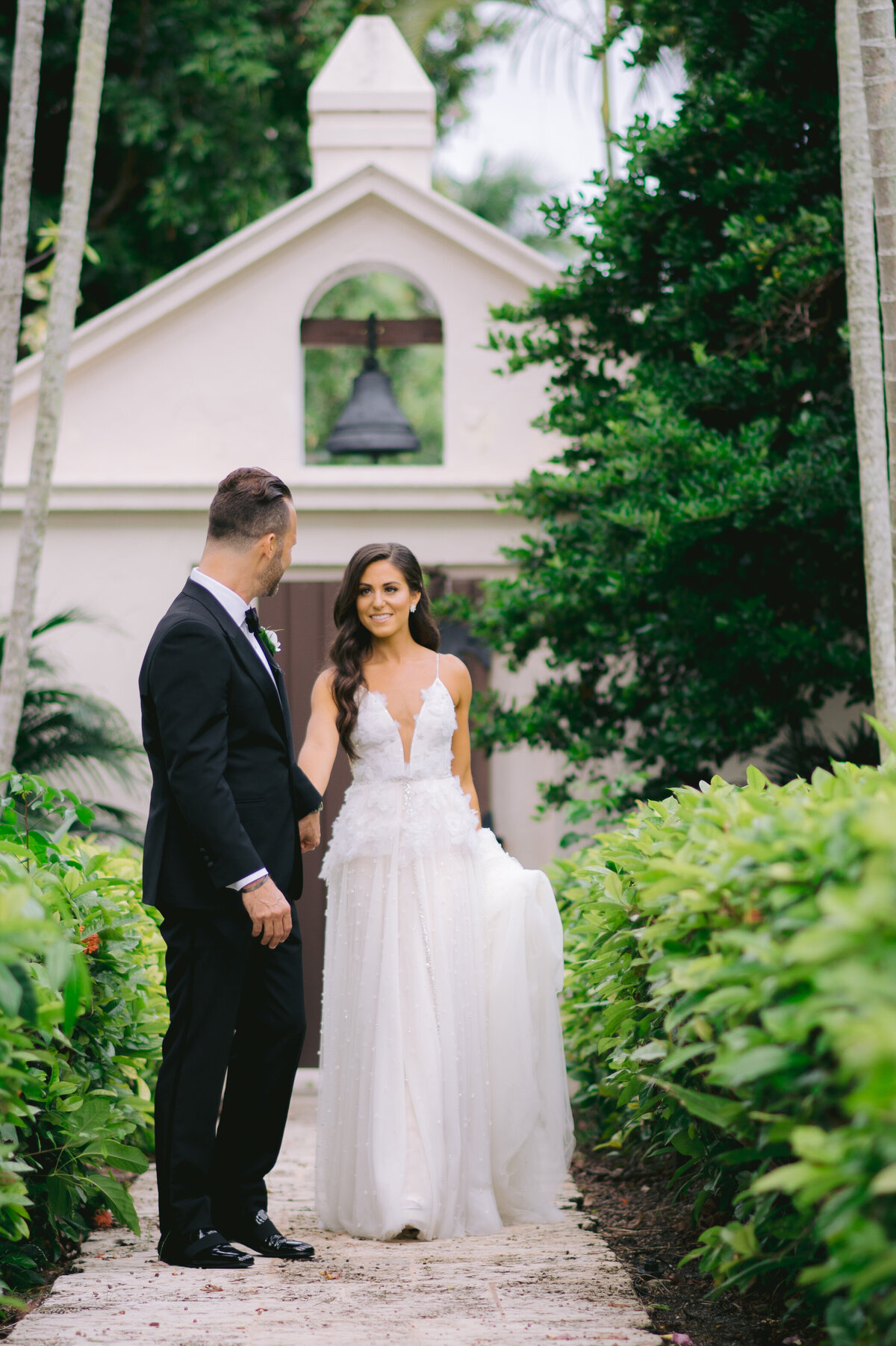 Groom and bride sharing a loving glance outside a chapel surrounded by lush greenery, photographed by Rodrigo Varela Photography in Miami, Florida.