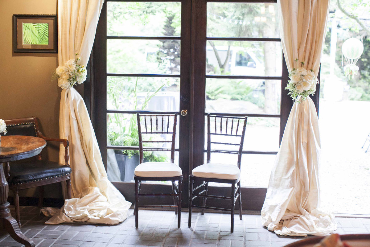window draped in ivory silk with two chivari chairs