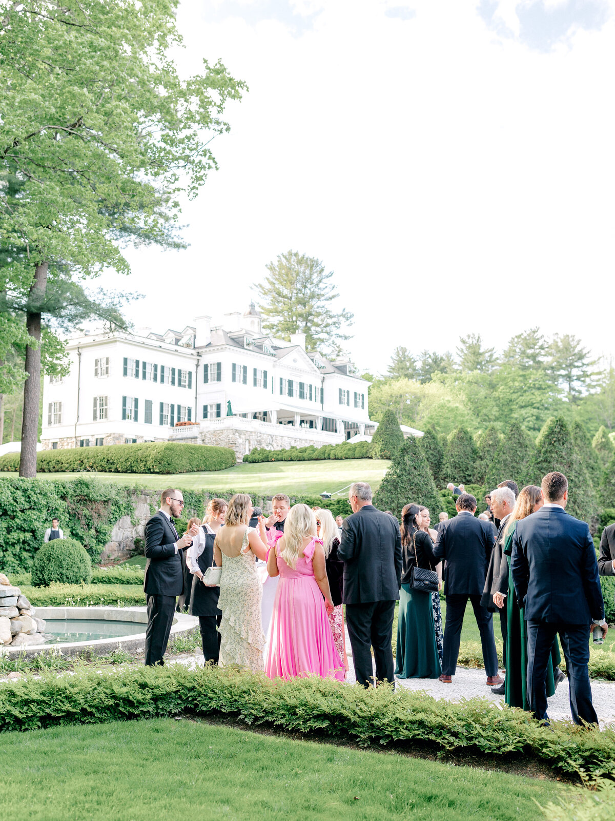 Guests stand in garden behind venue enjoying cocktail hour