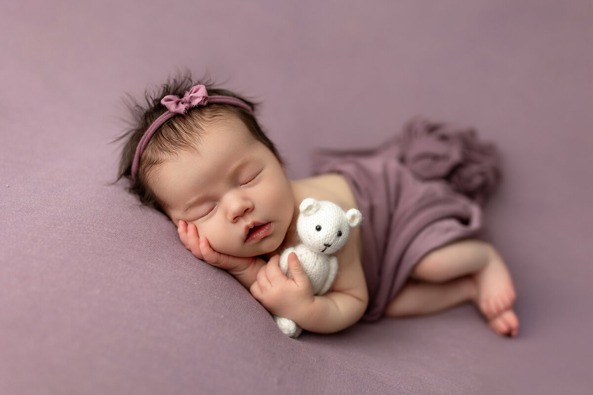 Newborn baby girl on purple with white bear