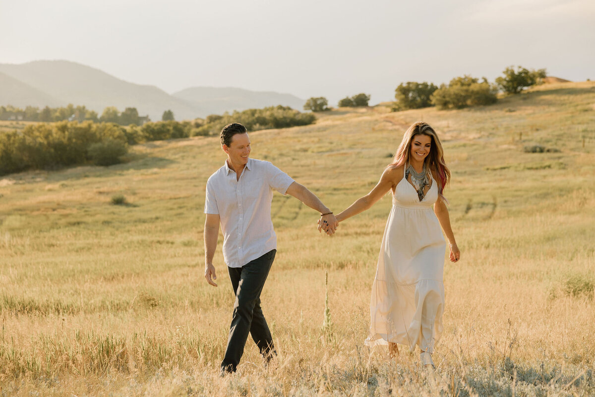 Couples walking through  pretty field in Colorado at Sunset