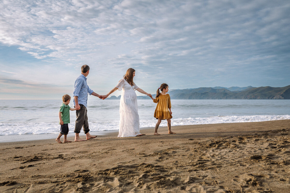 pregnant mother walking on San Francisco beach with her husband and two kids holding hands